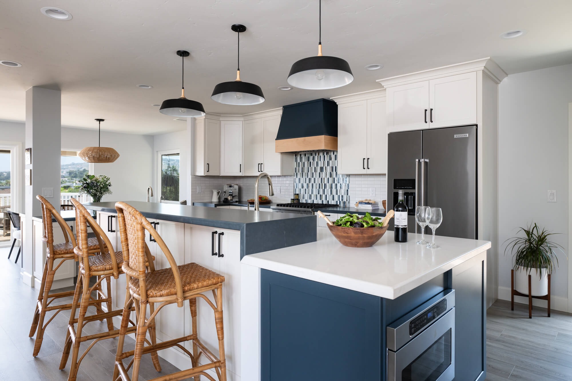 Wide hero of coastal modern kitchen with navy hood and rattan stools