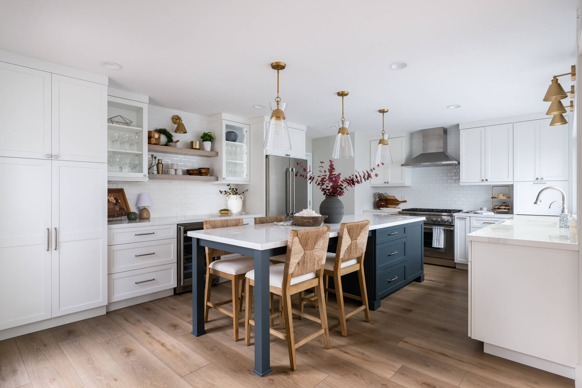 Wide hero of luxury kitchen with navy peninsula and brass pendants