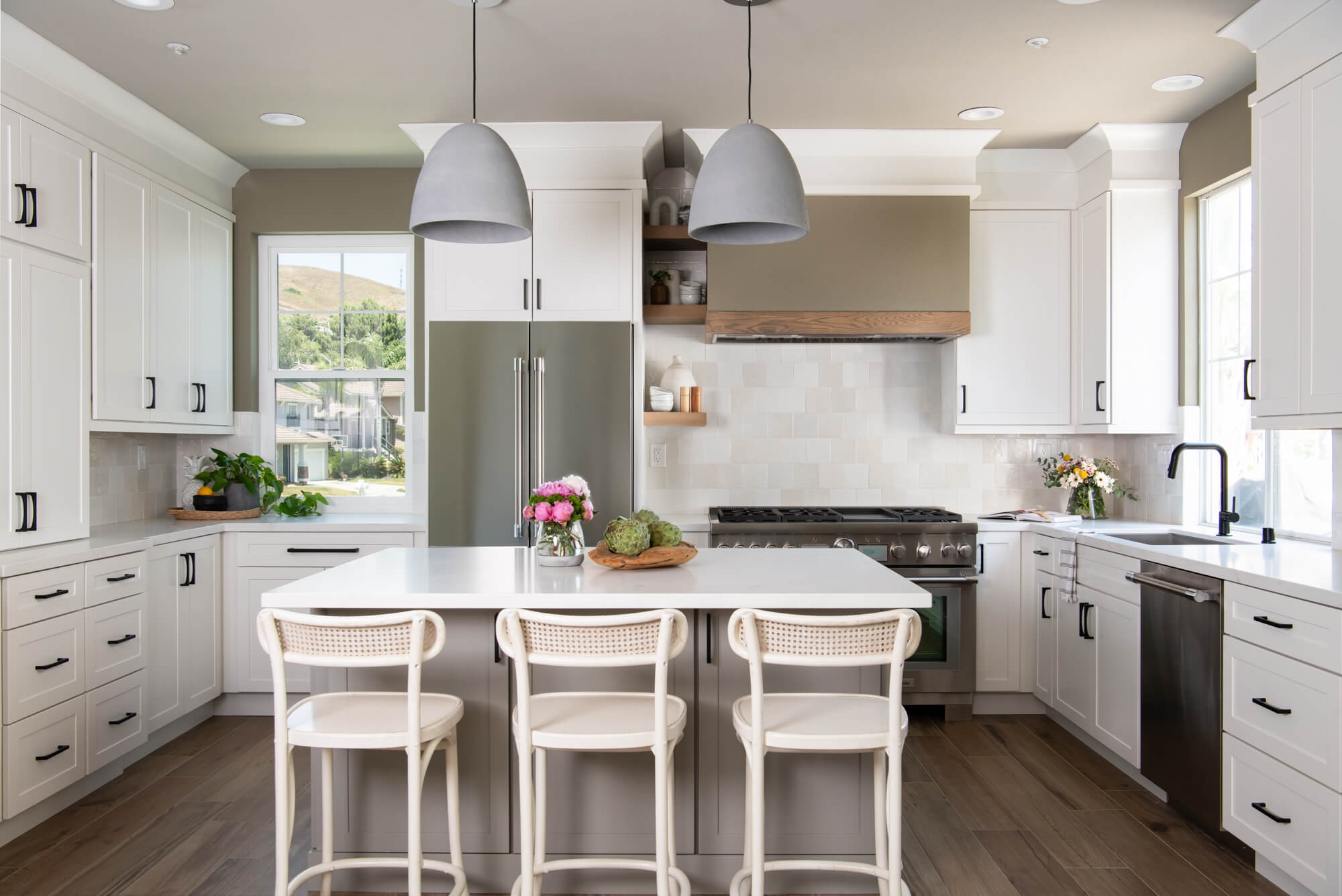 Bright and airy modern farmhouse kitchen remodel in Cumming GA with wood-banded range hood and cream cane stools