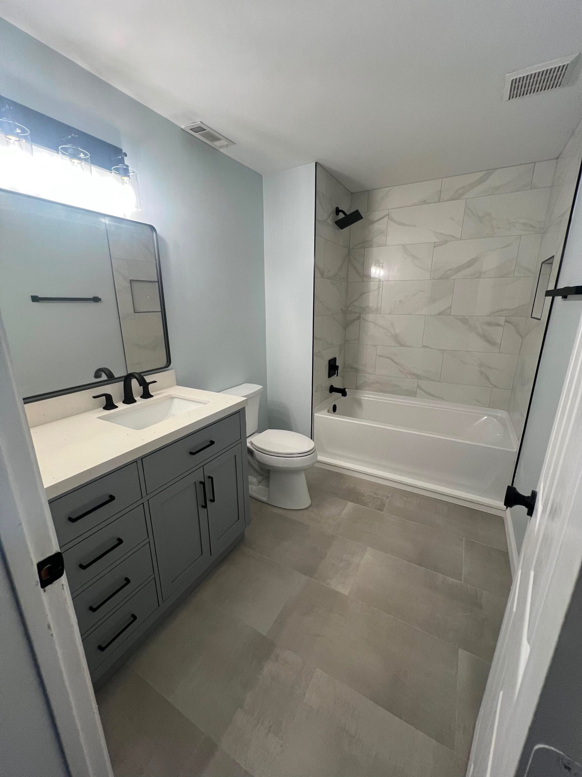 Bathroom remodel by Interior Transformation Remodeling in Metro Atlanta with grey shaker vanity marble-look tub surround and matte black fixtures