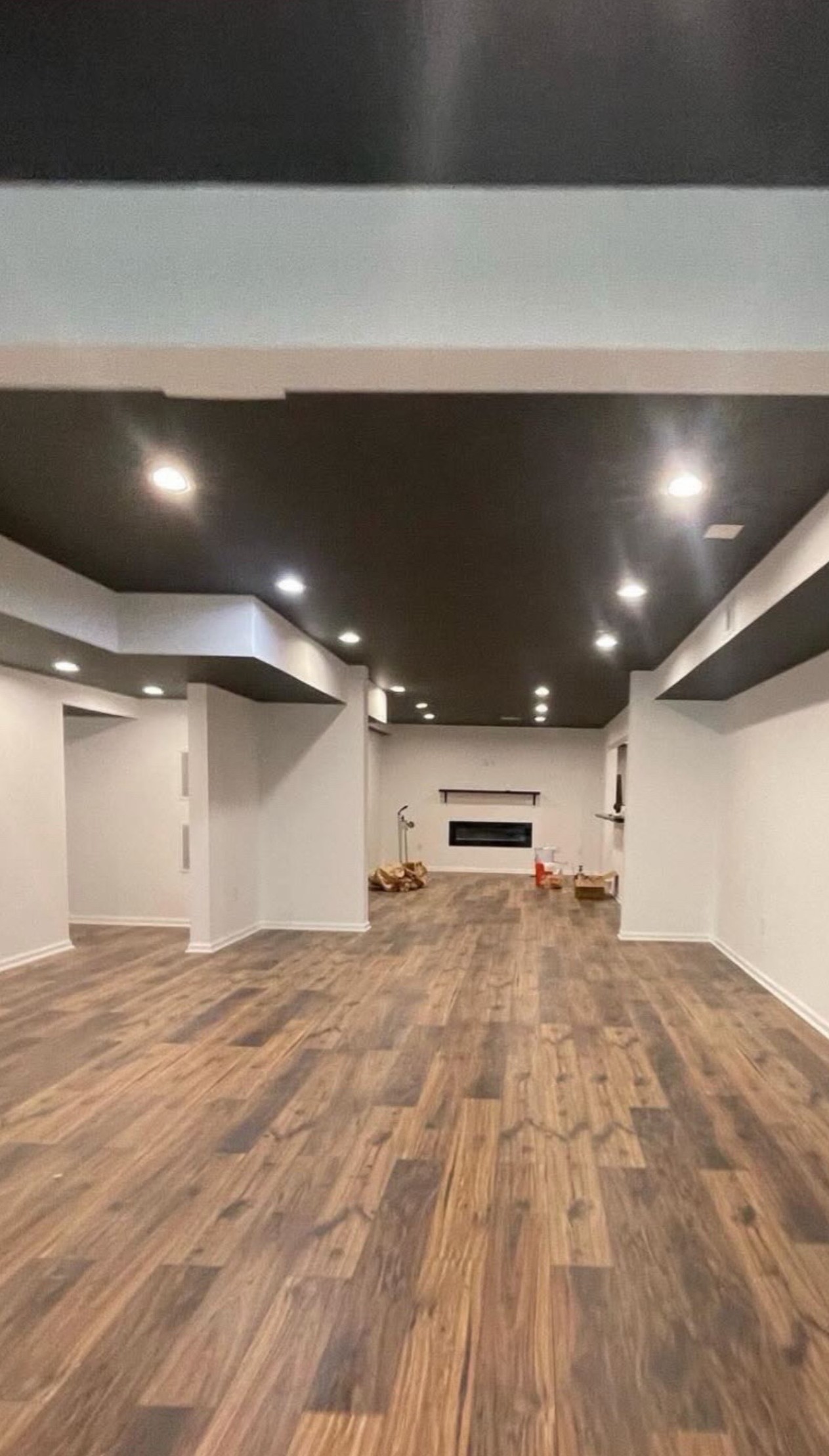 Finished basement after remodel with dark ceiling, white walls, hardwood floors, and stone fireplace