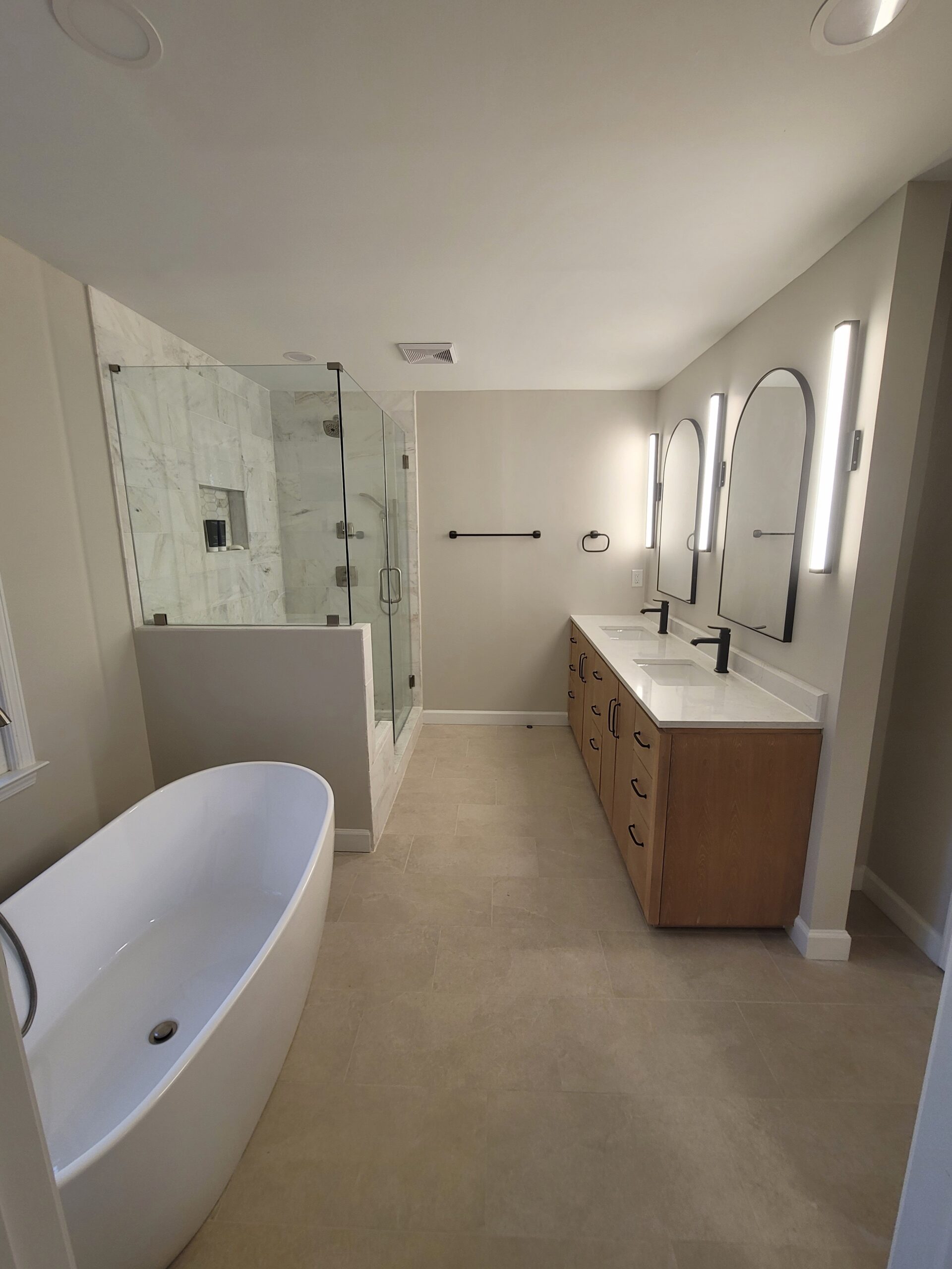 Master bathroom after remodel with freestanding soaker tub, marble shower, wood double vanity, and arched mirrors