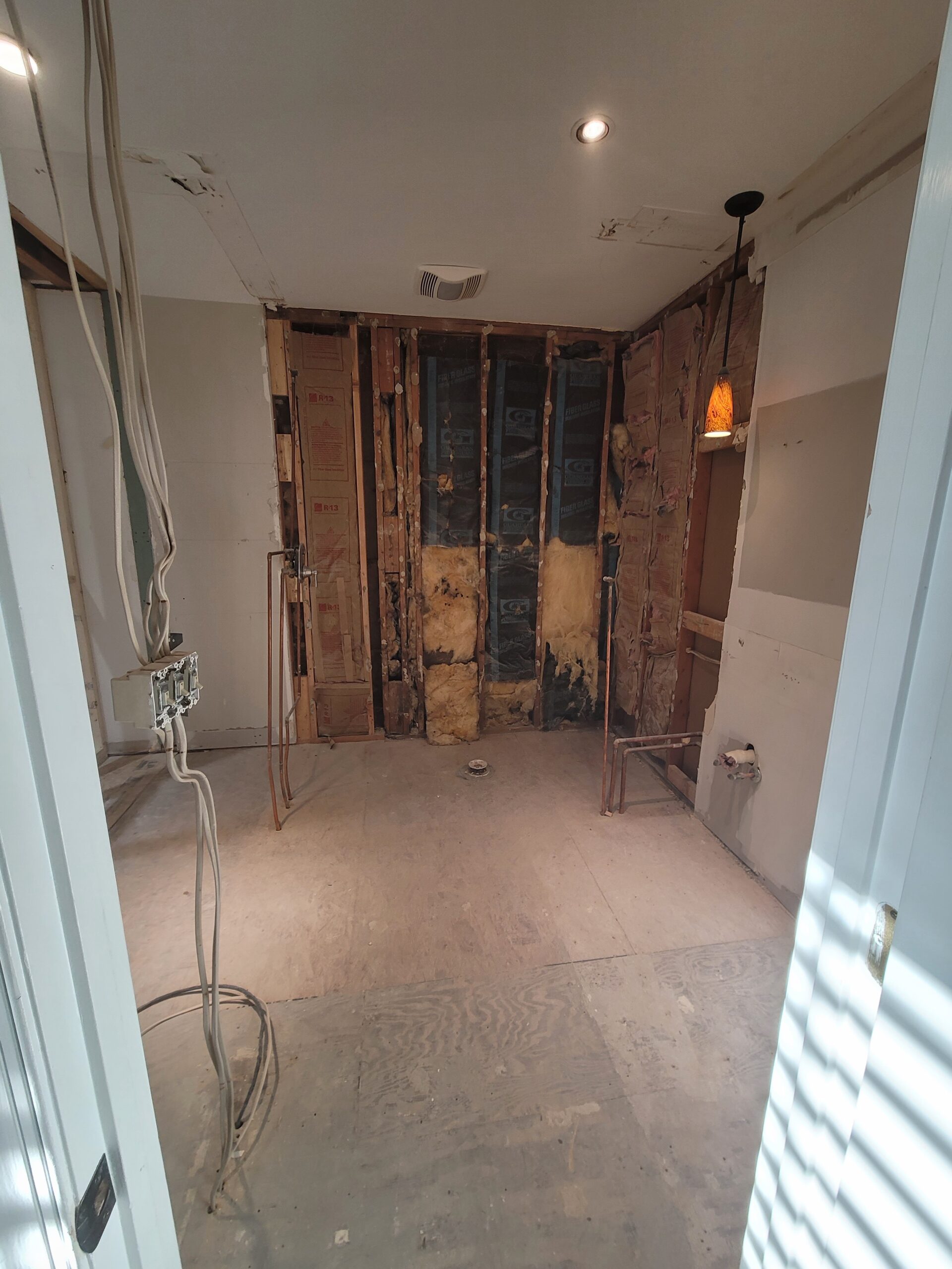 Master bathroom before remodel demoed down to studs, insulation, and rough plumbing