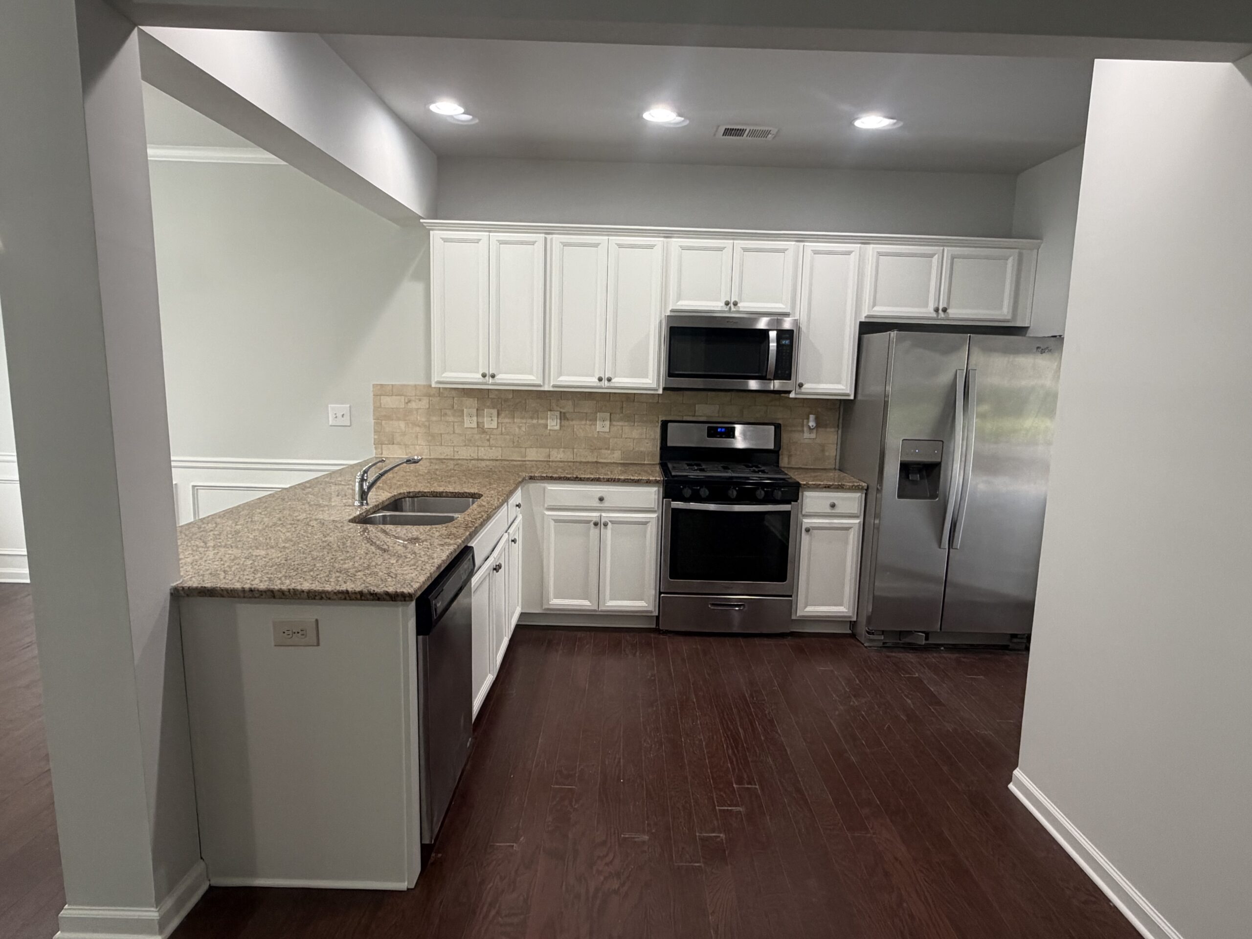 Kitchen after cabinet refinish with clean white cabinets and granite countertops