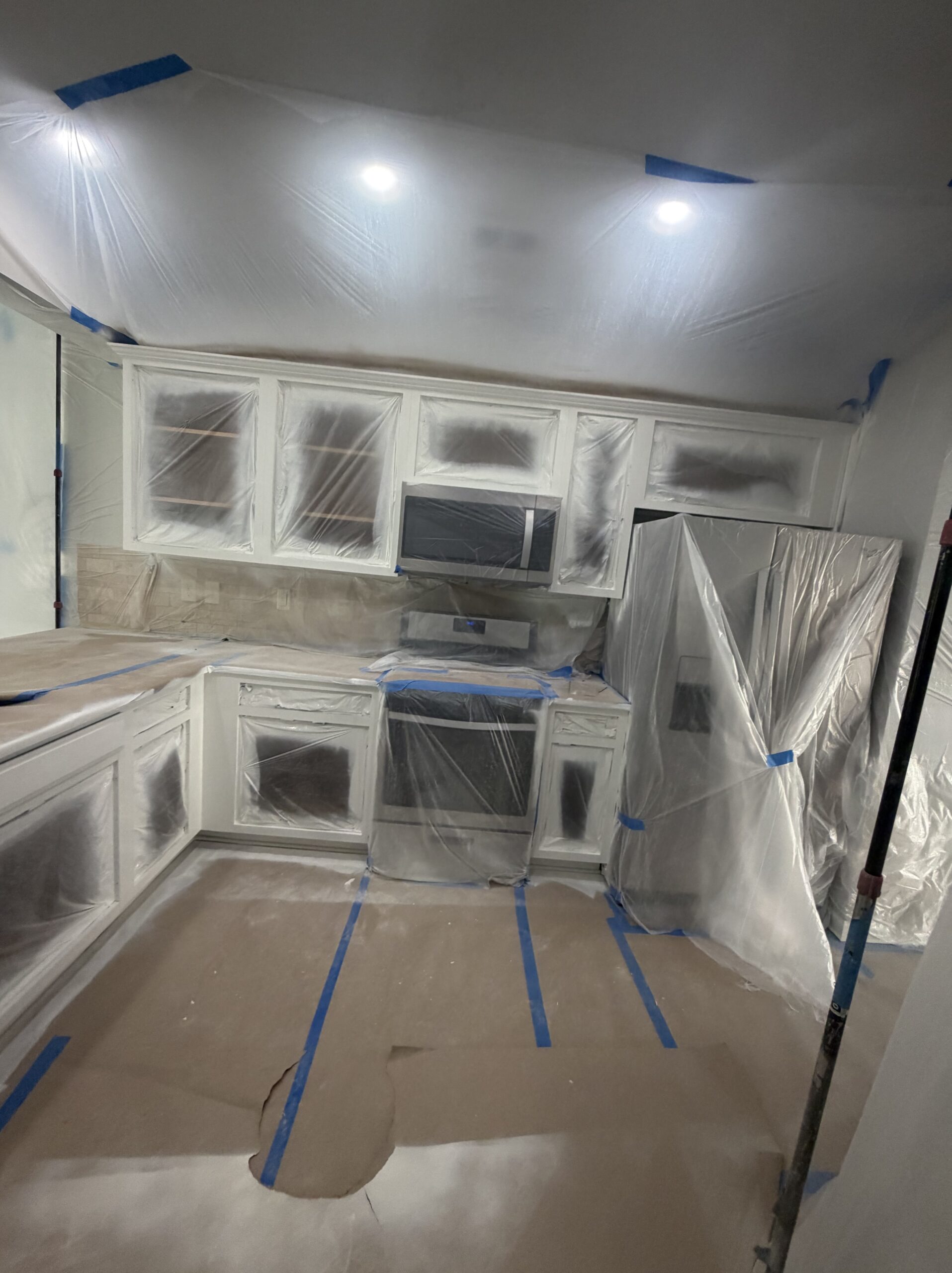 Kitchen during cabinet refinish with plastic sheeting and paint prep