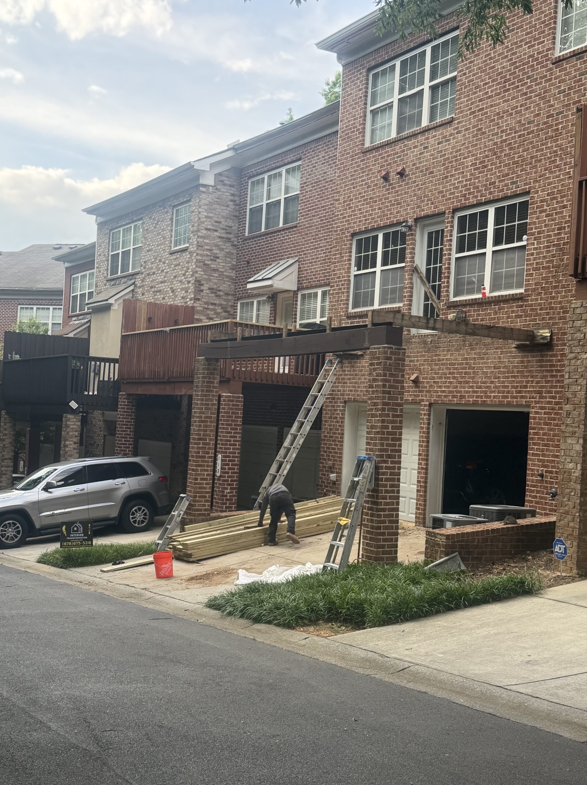 Brick townhouse before new deck install — old deck removed and fresh pressure-treated lumber staged on the driveway